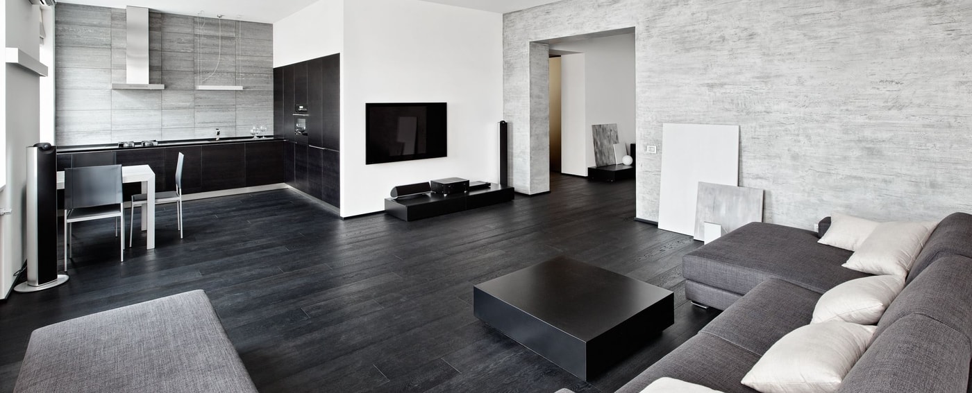 A living room with dark timber flooring with black sofa and white cushions. 