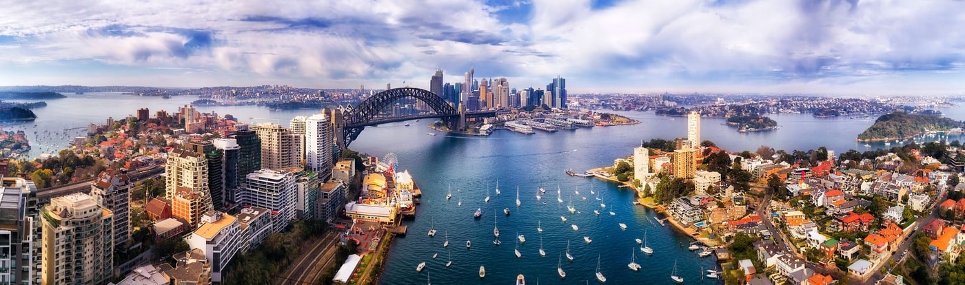 An aerial view of the Sydney CBD with view of the harbour bridge, the city buildings and the surrounding sparkling water.